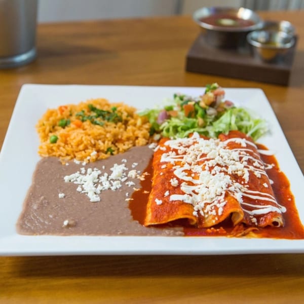 El Taquito's enchiladas with red sauce, rice, refried beans, and salad on a white plate.