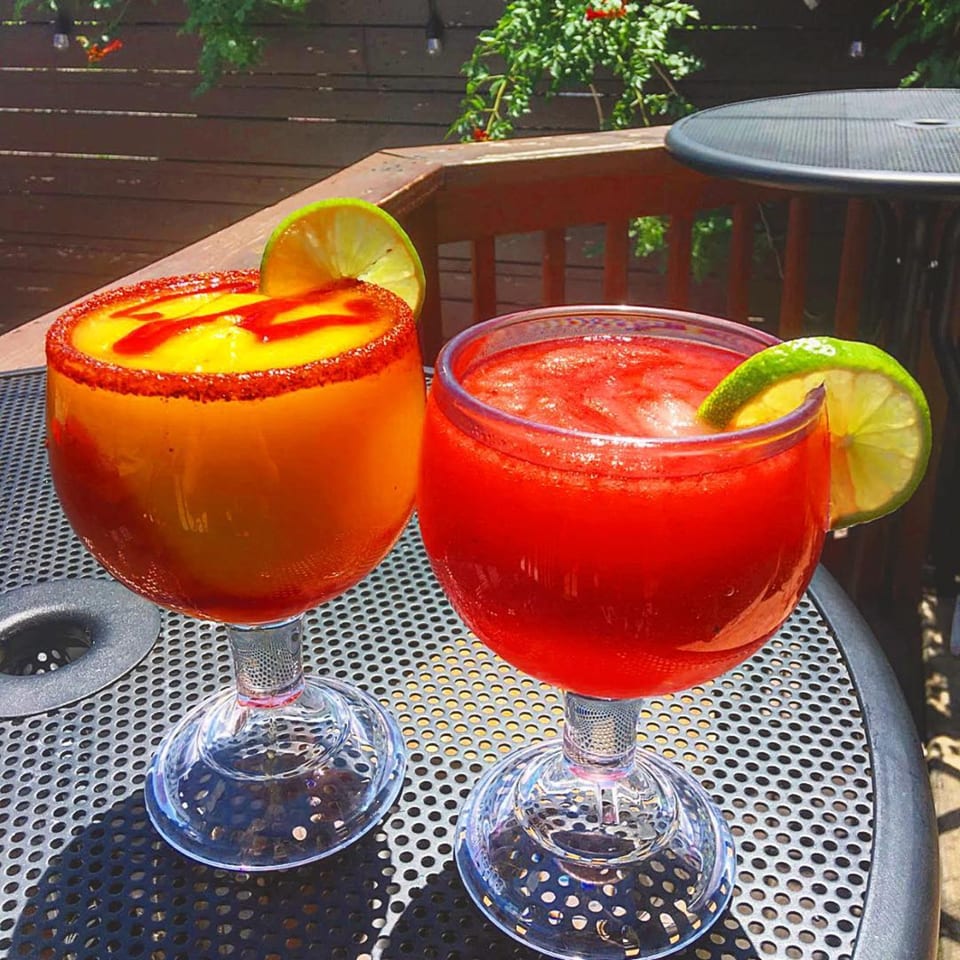 Two colorful El Taquito margaritas, one mango and one strawberry, on an outdoor patio table.