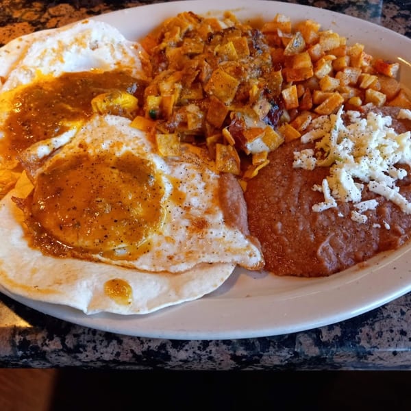 Huevos Rancheros with two fried eggs, salsa, refried beans, and diced potatoes on a white plate.