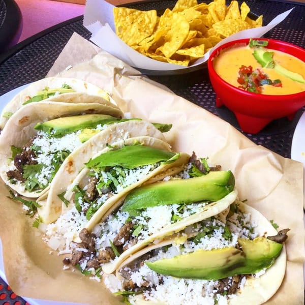 Four El Taquito tacos with meat, cheese, cilantro, and avocado, alongside chips and queso.