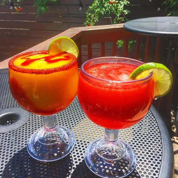 Two colorful margaritas, one yellow and one red, with lime slices on an outdoor patio table.