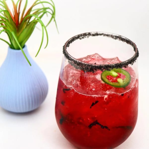 A vibrant red El Taquito margarita with a black salt rim and a jalapeño slice.