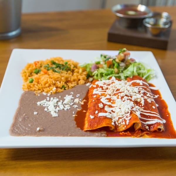 El Taquito's enchiladas with red sauce, rice, refried beans, and salad on a white plate.